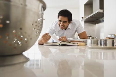 A picture of a man cooking using a recipe from a cookbook.