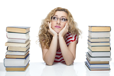 A picture of a student sitting between two large stacks of books gazing off into the distance.