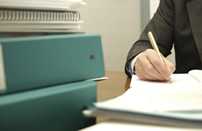 A person writing a paper while surrounded by stacks of research.